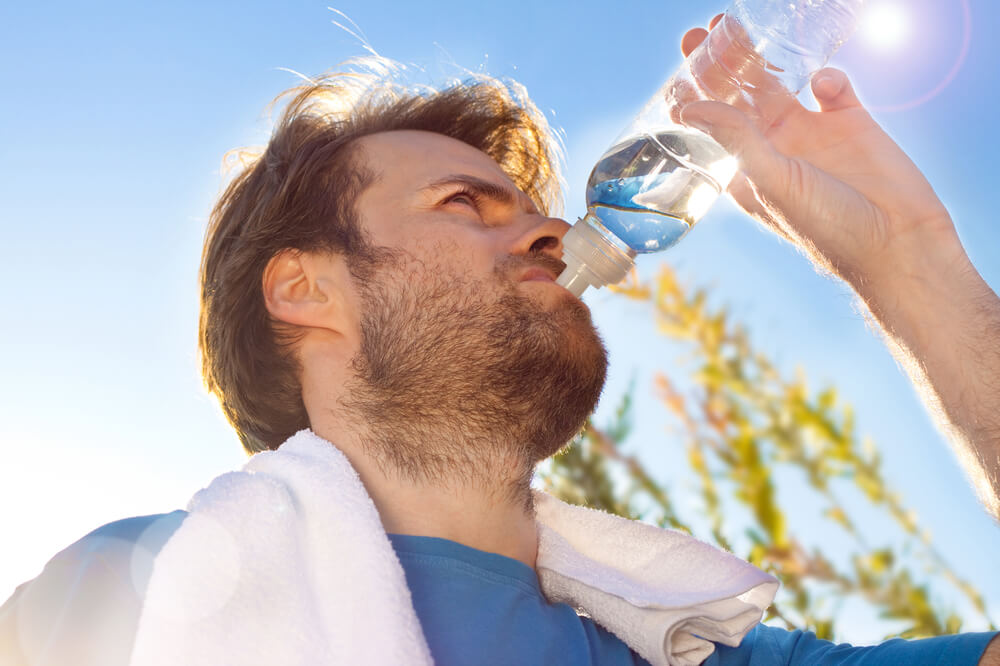 Forty years old caucasian active man drinking water and having a rest after workout during sunny summer day